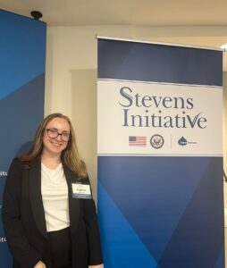 A young adult stands in front of a banner that says "Stevens Initiative."